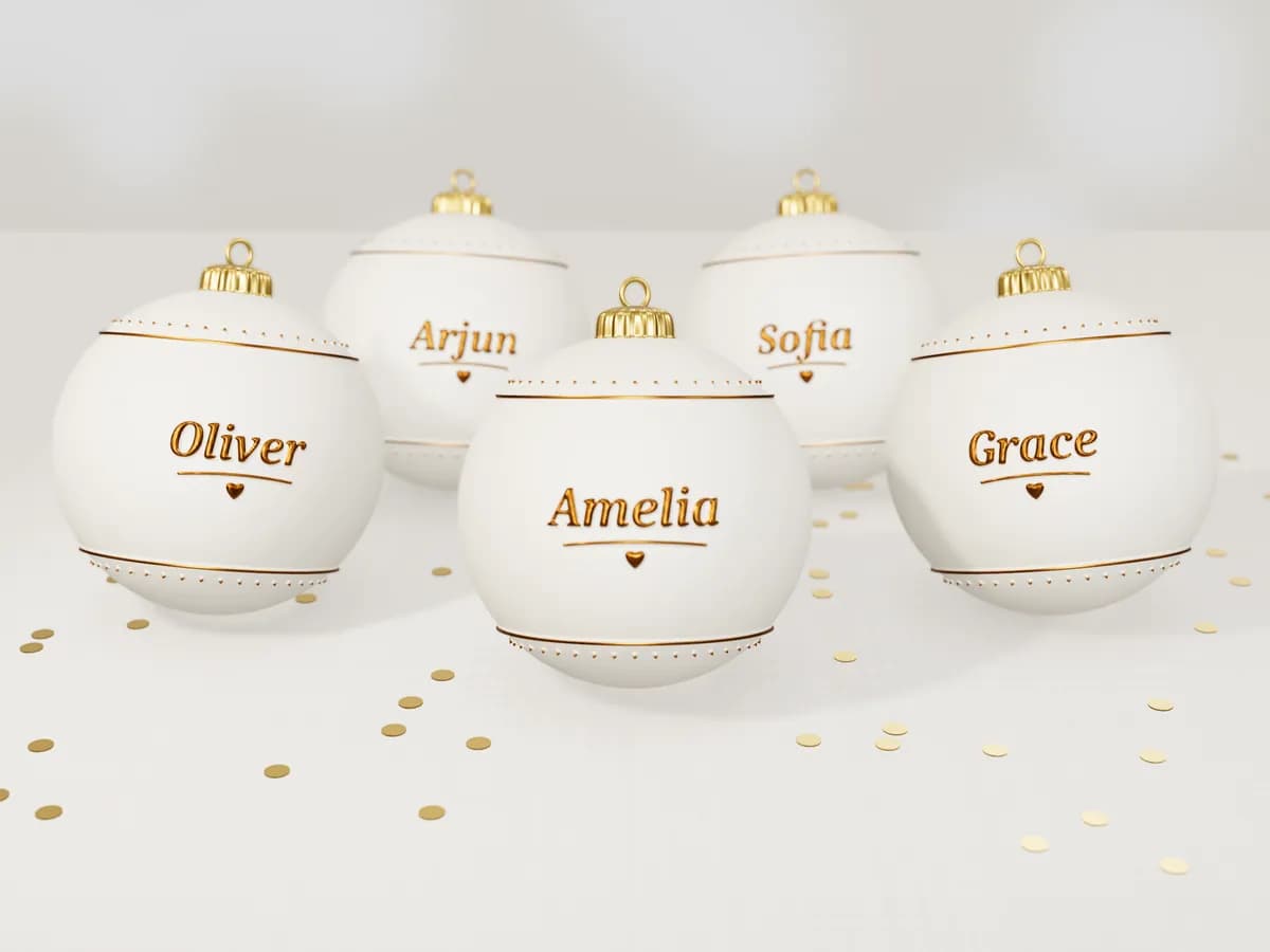 Ivory wedding-favour baubles, each with a guest's name in raised gold letters, on a linen tablecloth