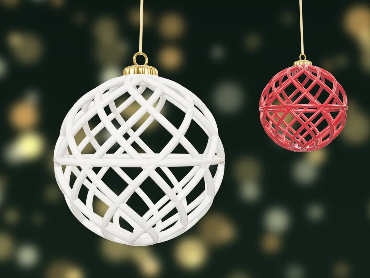 Two openwork baubles of twisting lattice, one ivory and one red, hanging against fairy lights