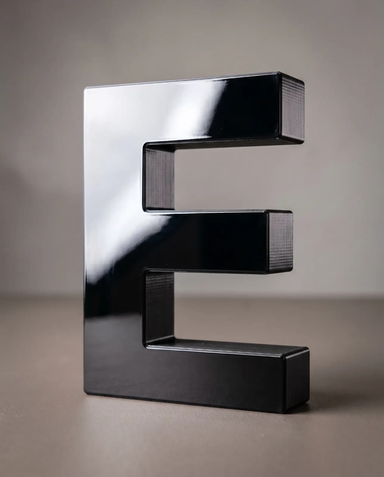 A glossy black 3D-printed letter E, catching the light
