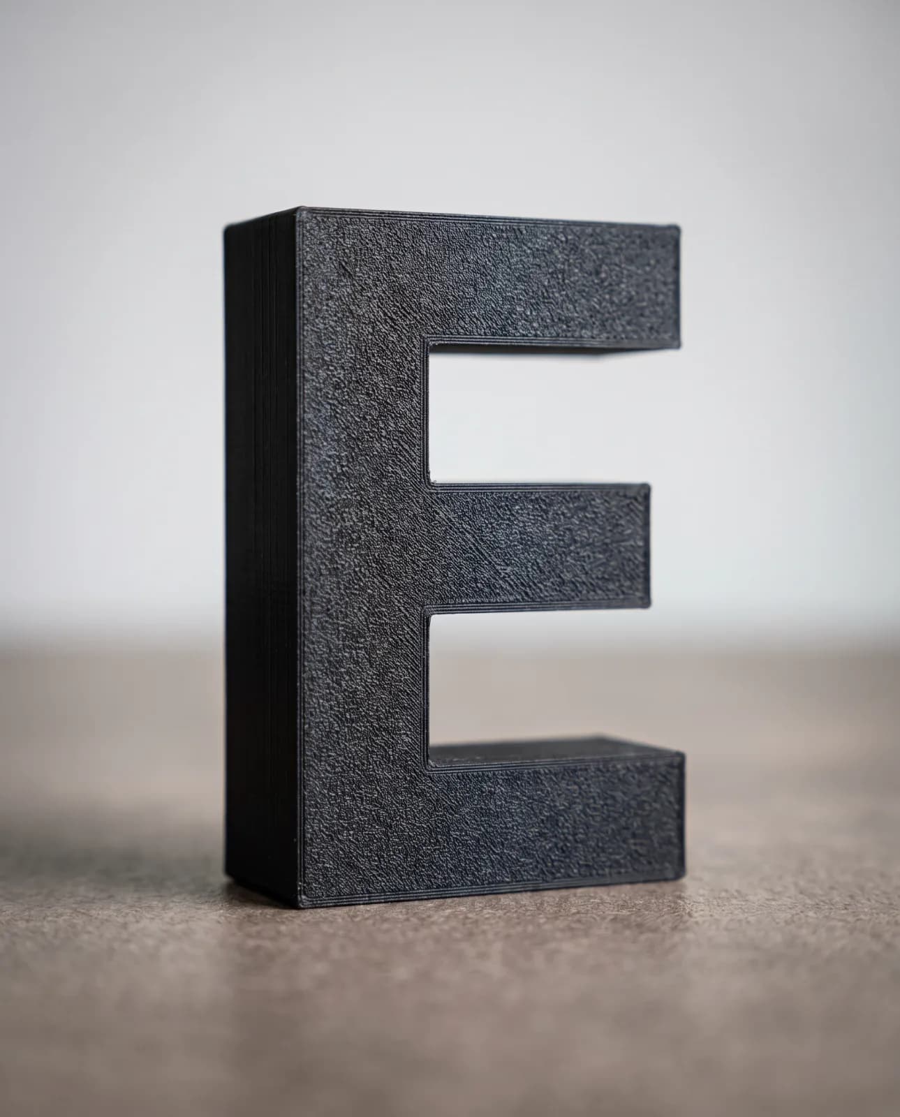 A black 3D-printed letter E with a fine, even textured surface