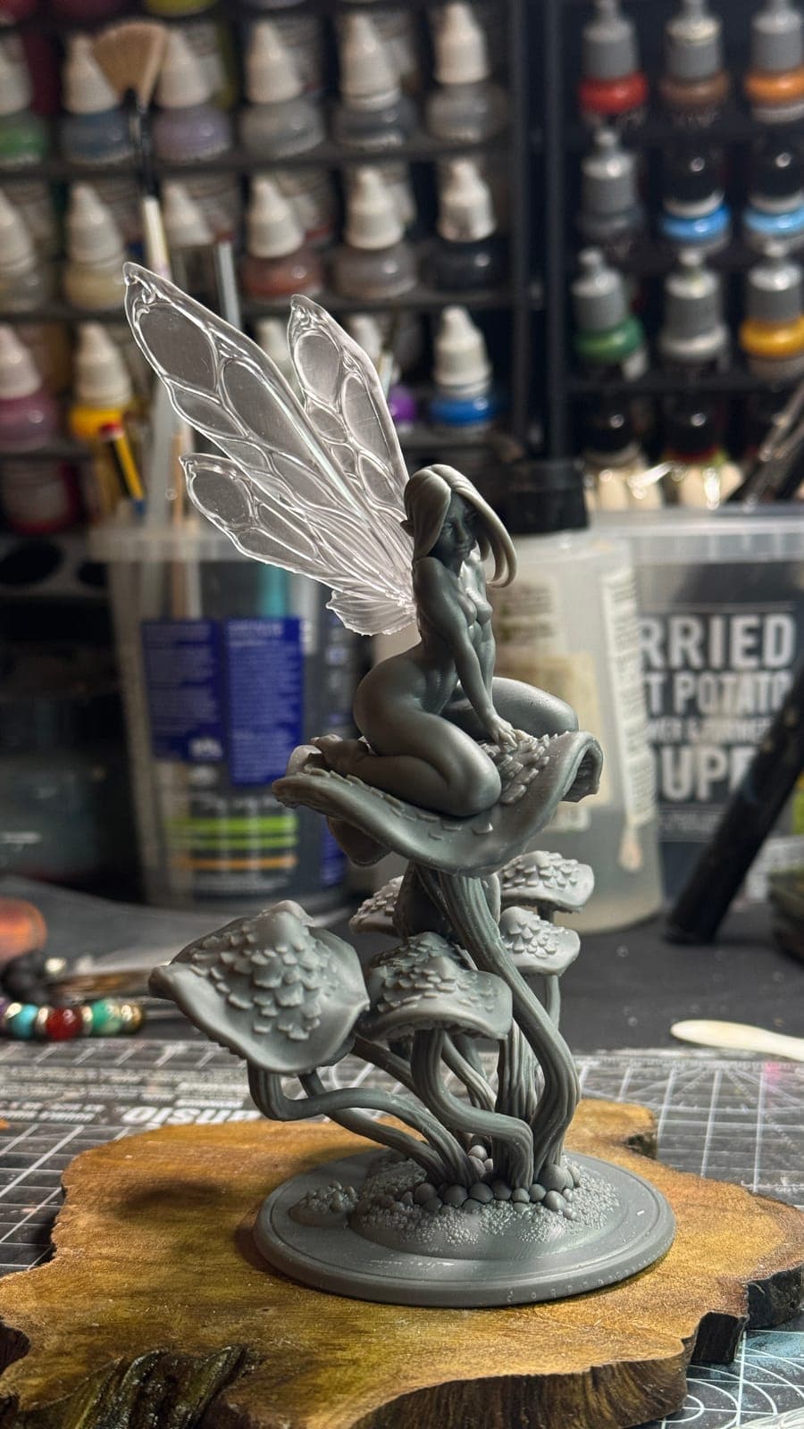 An unpainted resin fairy on mushrooms, on a wooden base at the workbench
