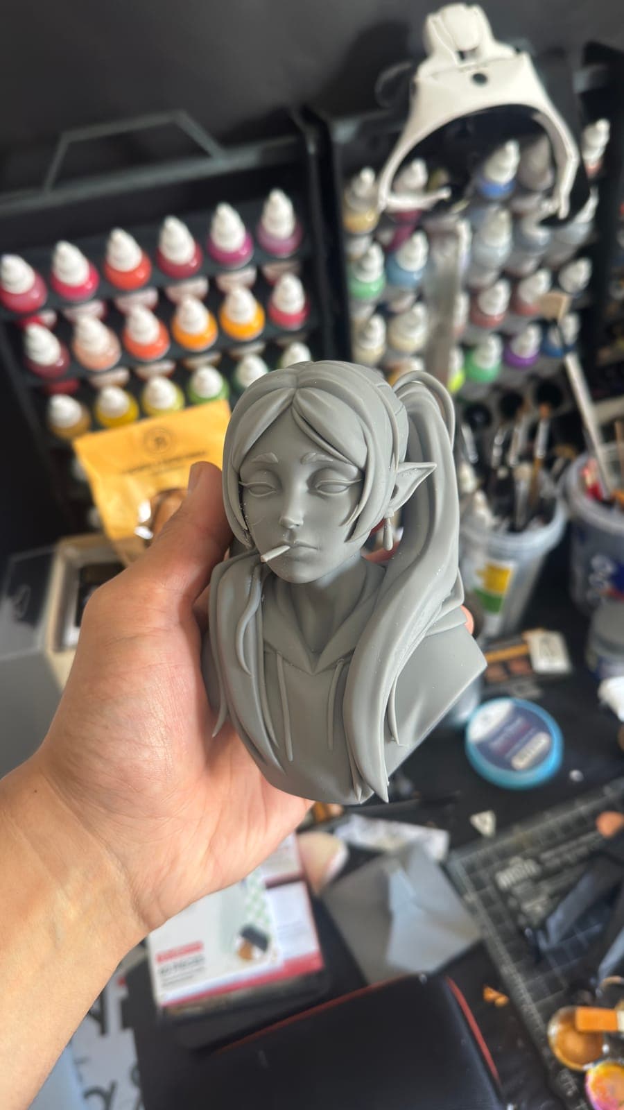 An unpainted resin bust of a girl, held in front of the paint rack