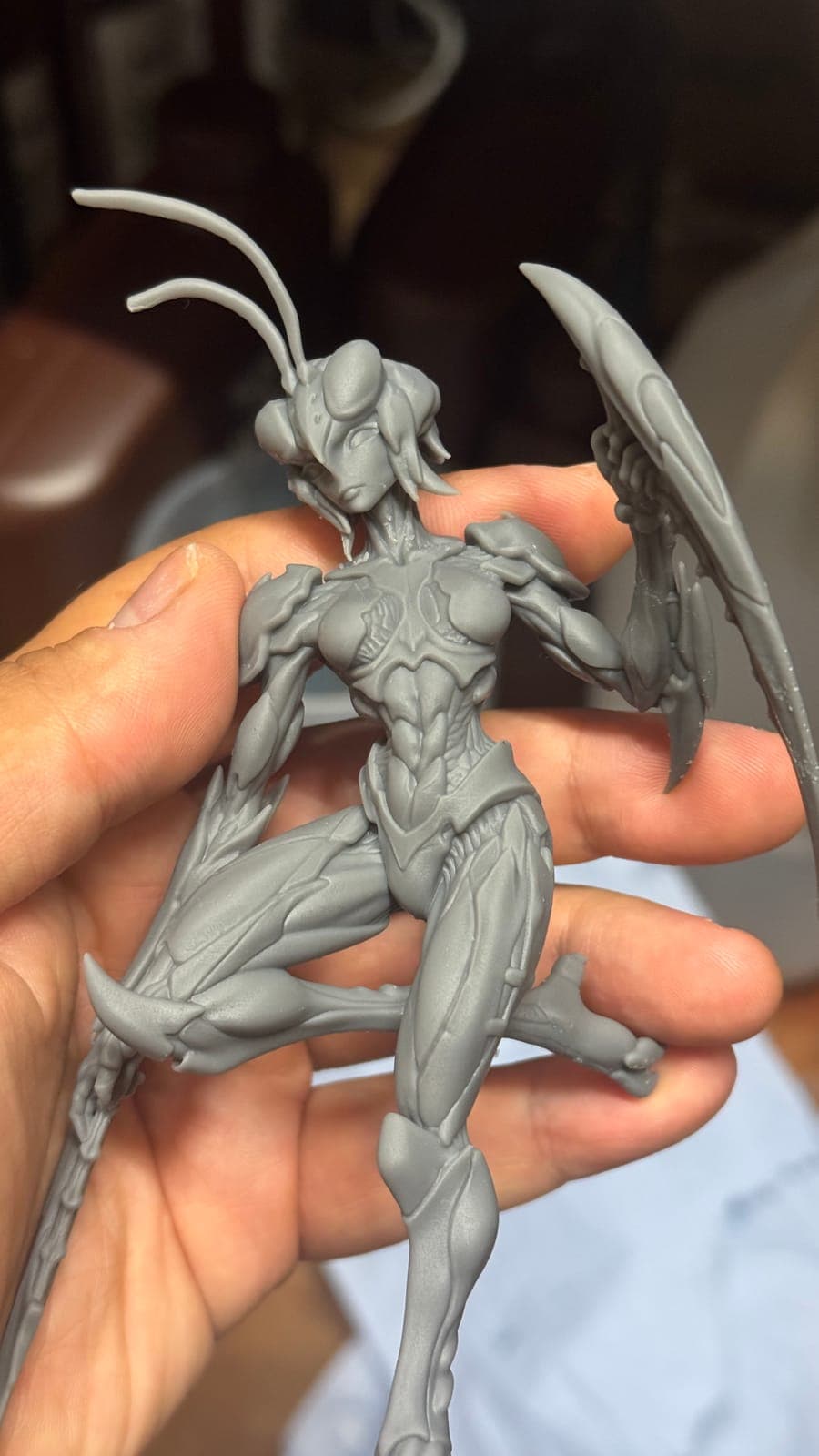 An unpainted resin print of a slender insect warrior with blades, held in the hand