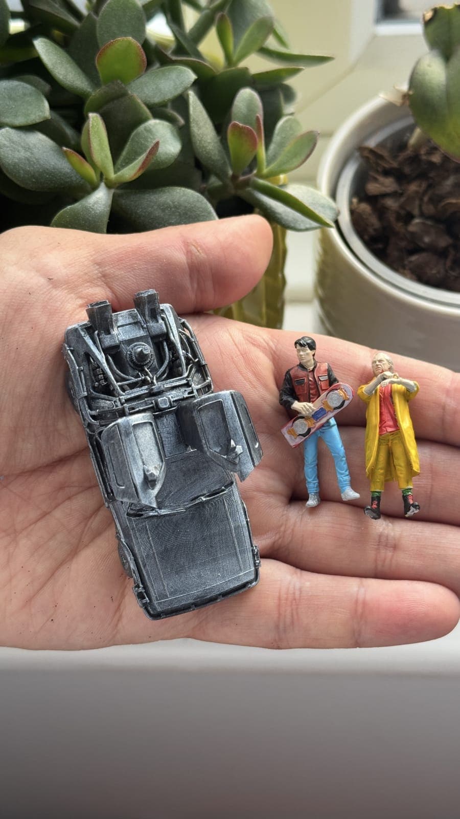 A miniature resin-printed vehicle and two tiny painted figures held in the palm