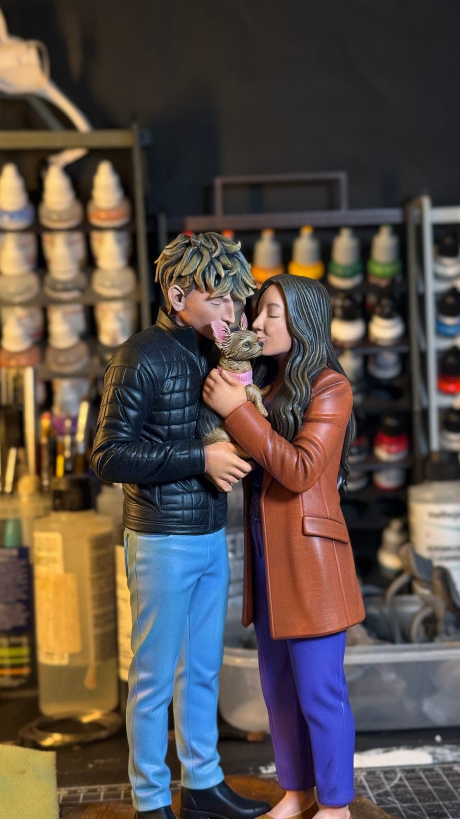 A hand-painted resin figurine of a couple embracing, in front of the paint rack