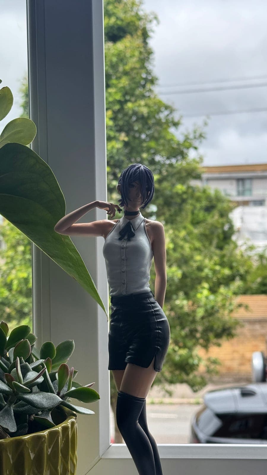 A hand-painted resin figurine of a woman in a white shirt and black skirt, standing by a window
