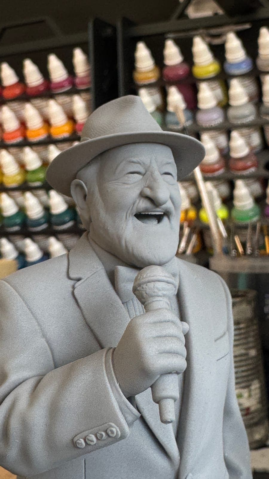 An unpainted resin bust of a laughing man in a hat, singing into a microphone