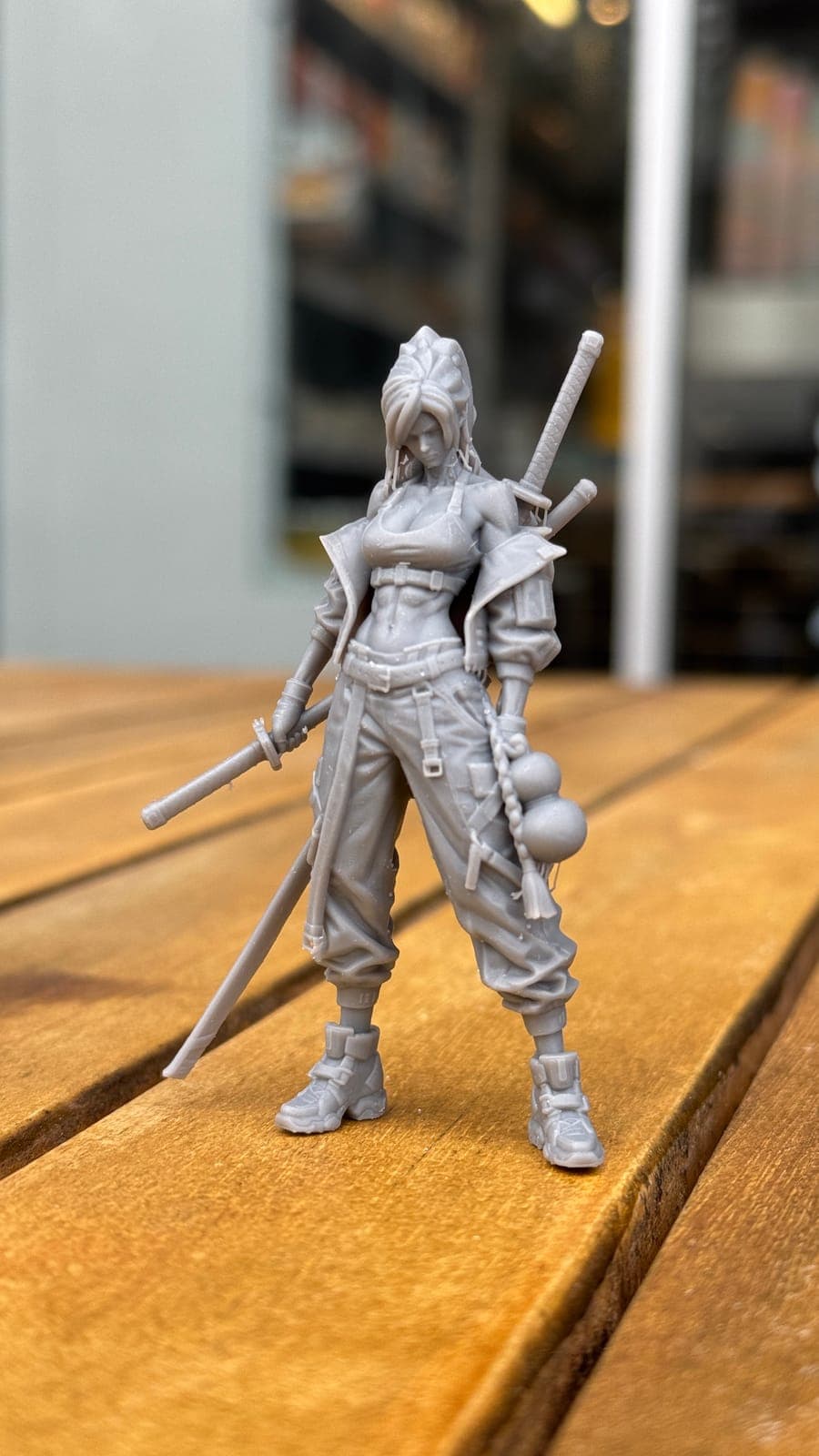 An unpainted resin print of a woman with swords, standing on a wooden table