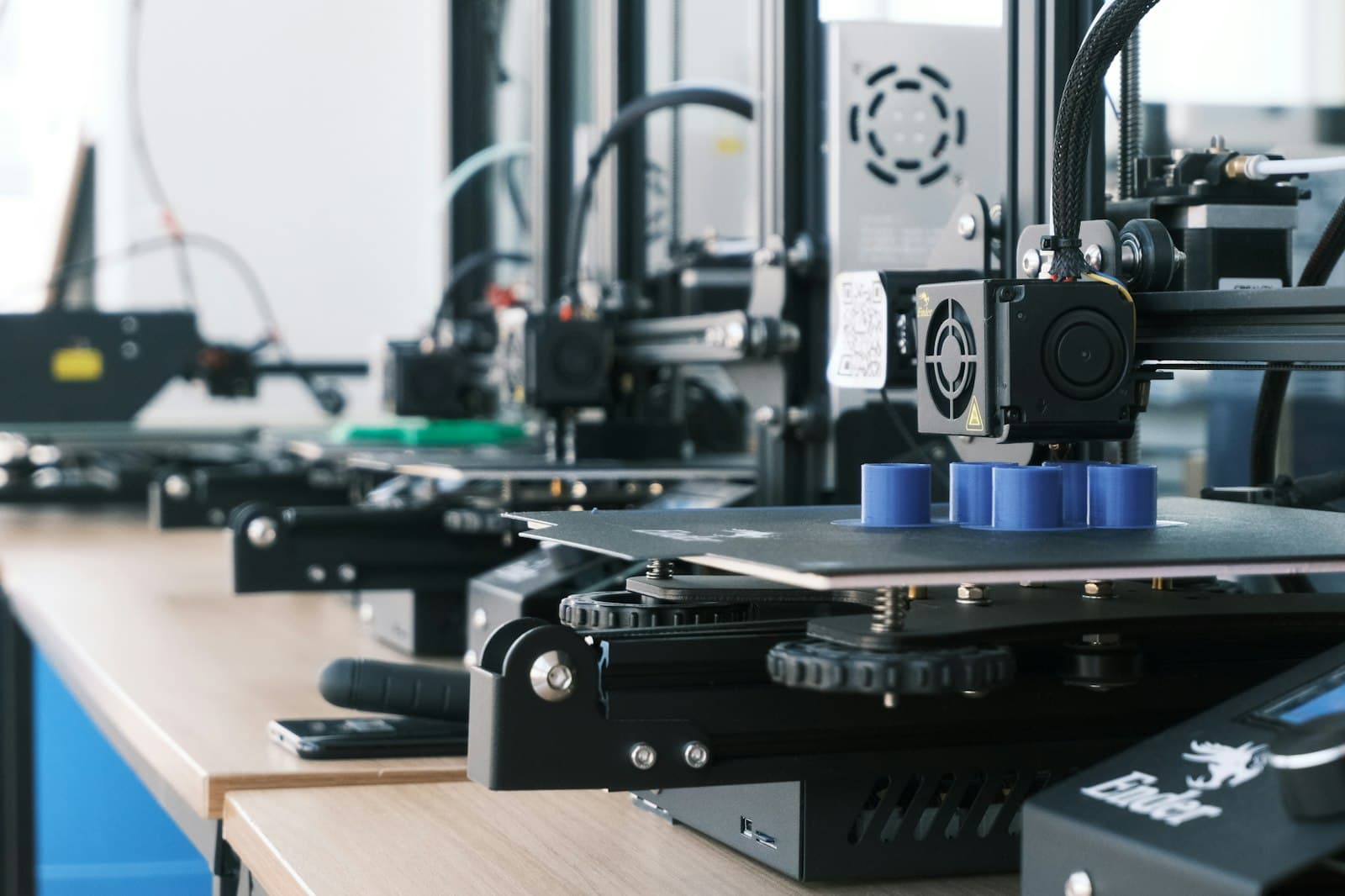 A row of FDM printers producing the same blue part
