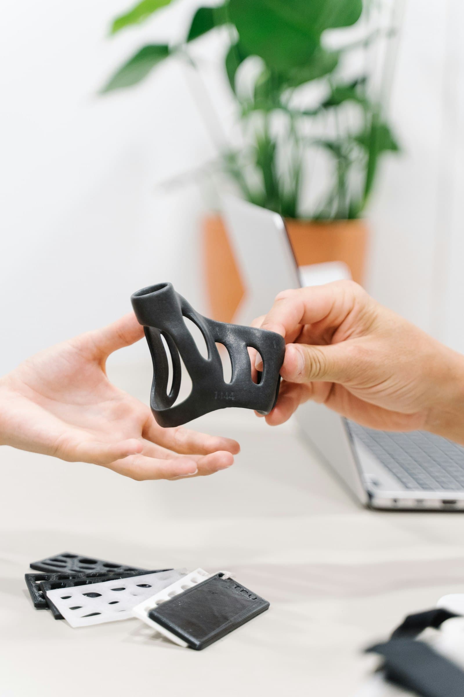 Two hands passing a black 3D-printed functional part