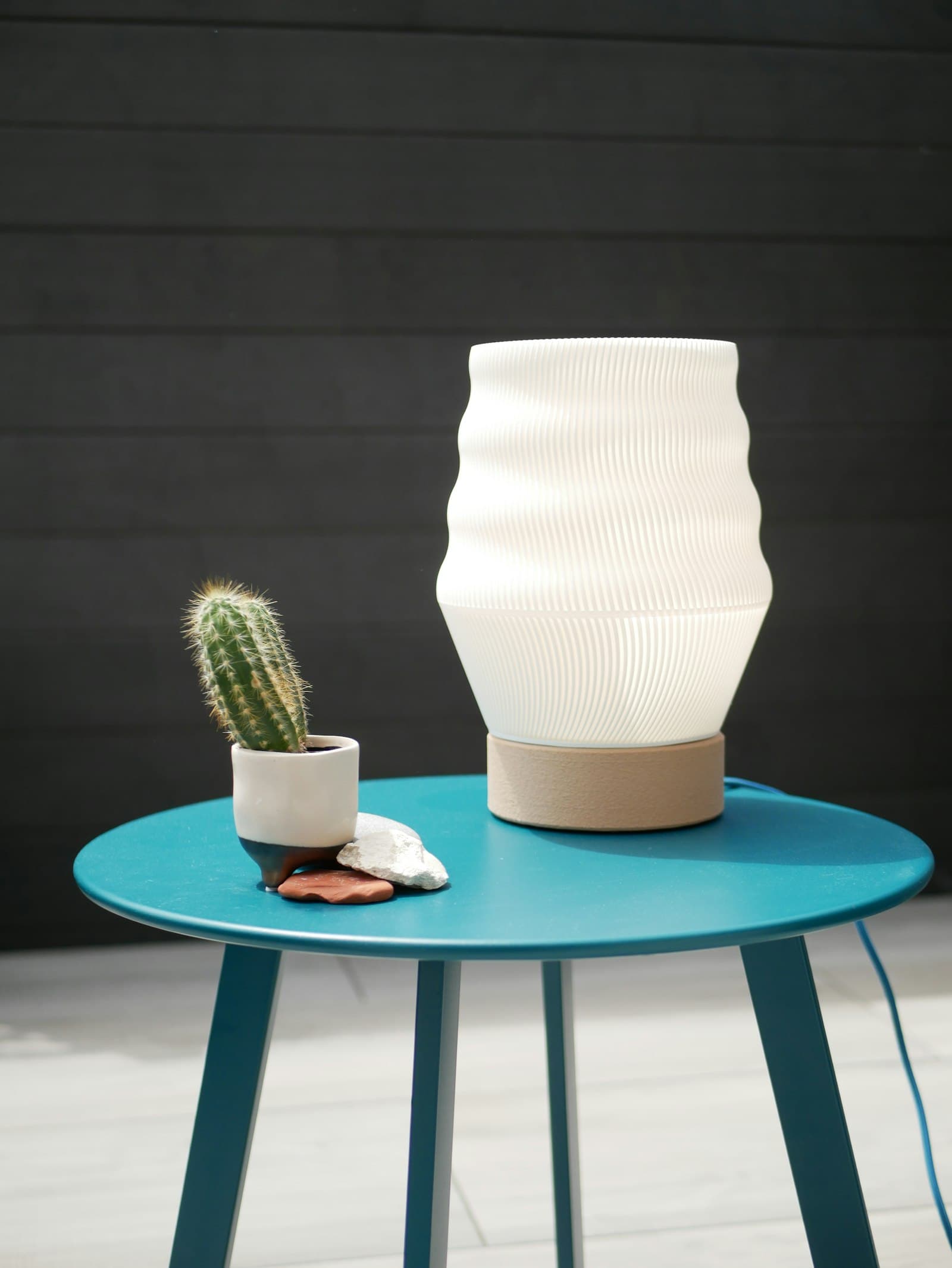 A ribbed 3D-printed lamp on a small table beside a potted cactus
