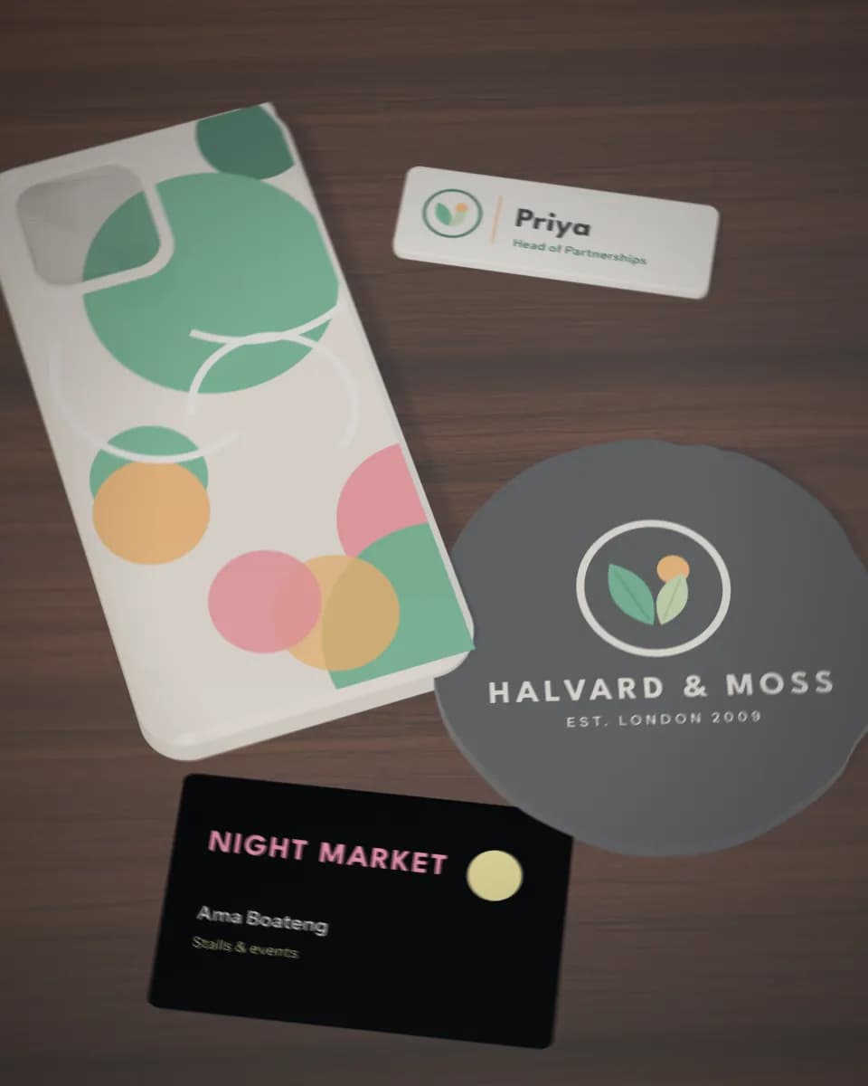 Flat printed pieces on a walnut desk: a phone case in bold colours, a slate coaster, a name badge and a black metal business card
