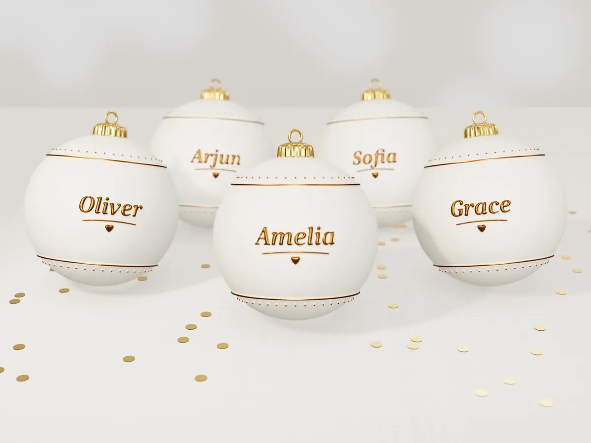 Ivory wedding-favour baubles, each with a guest's name in raised gold letters, on a linen tablecloth