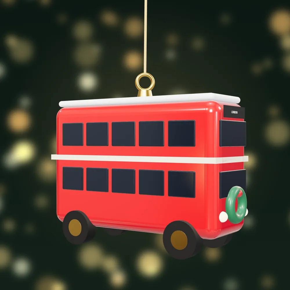 A glossy red London double-decker bus bauble with snow on its roof and a wreath on the front