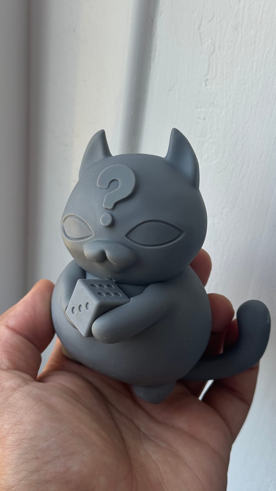 An unpainted resin print of a round cat figure, held in the hand