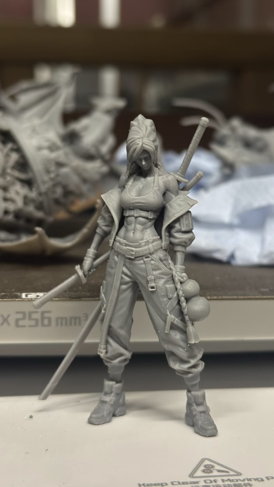 An unpainted resin figure of a sword-carrying woman on the printer build plate
