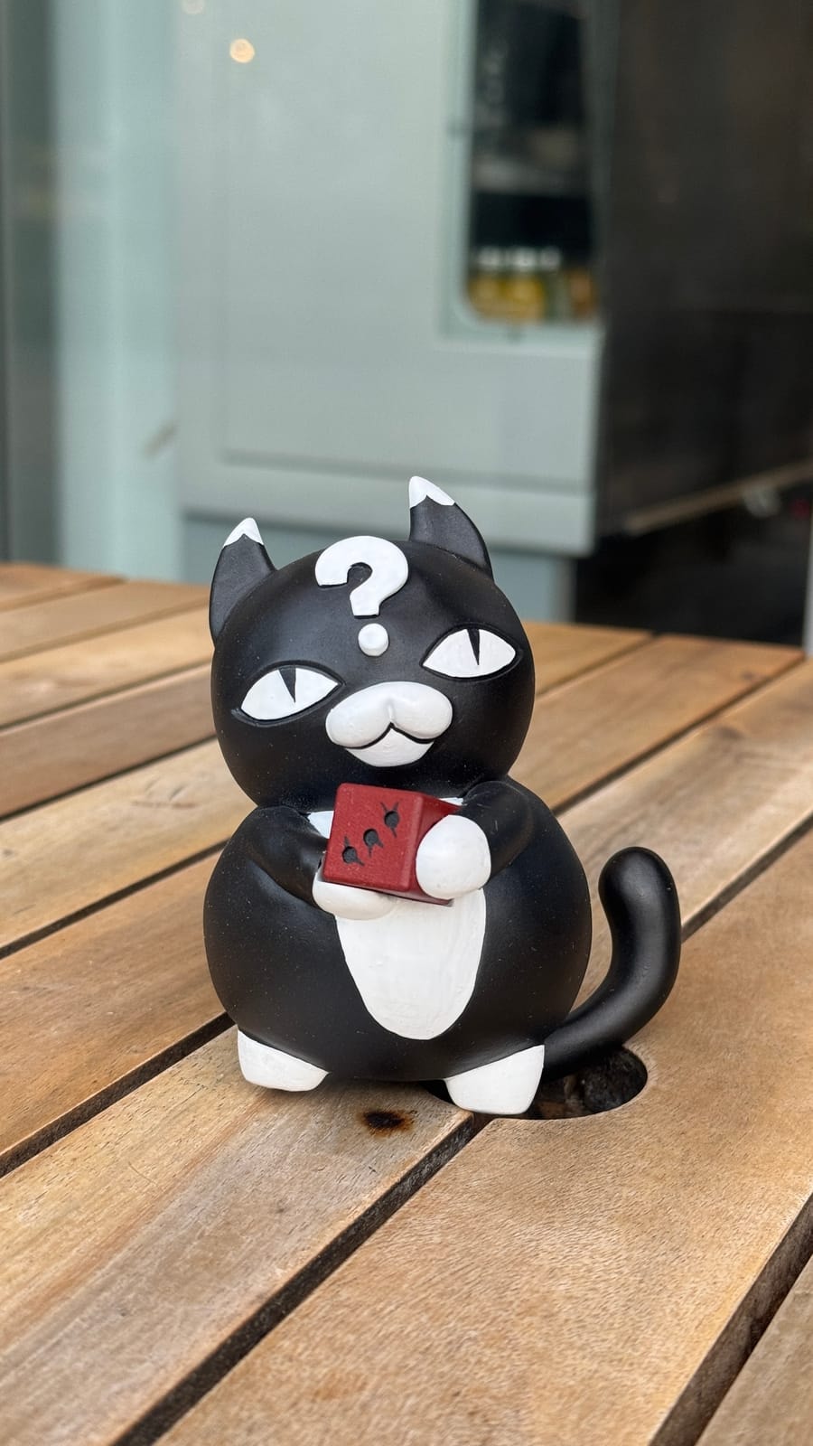 A glossy black and white painted cat figure with a question mark on its head, on a wooden table