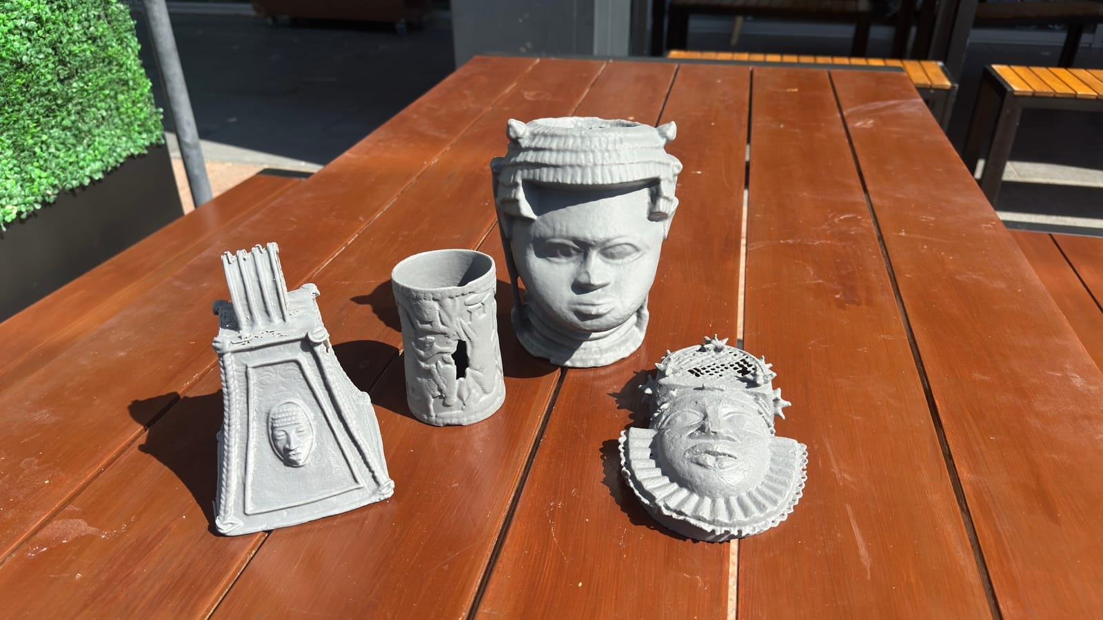 Unpainted resin prints of sculpted heads and a small relic on a wooden table