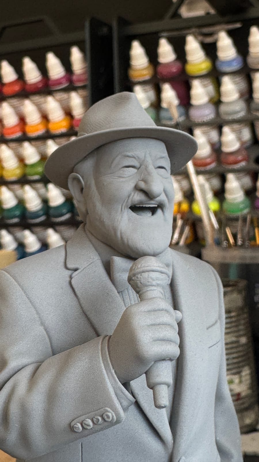 An unpainted resin bust of a laughing man in a hat, singing into a microphone