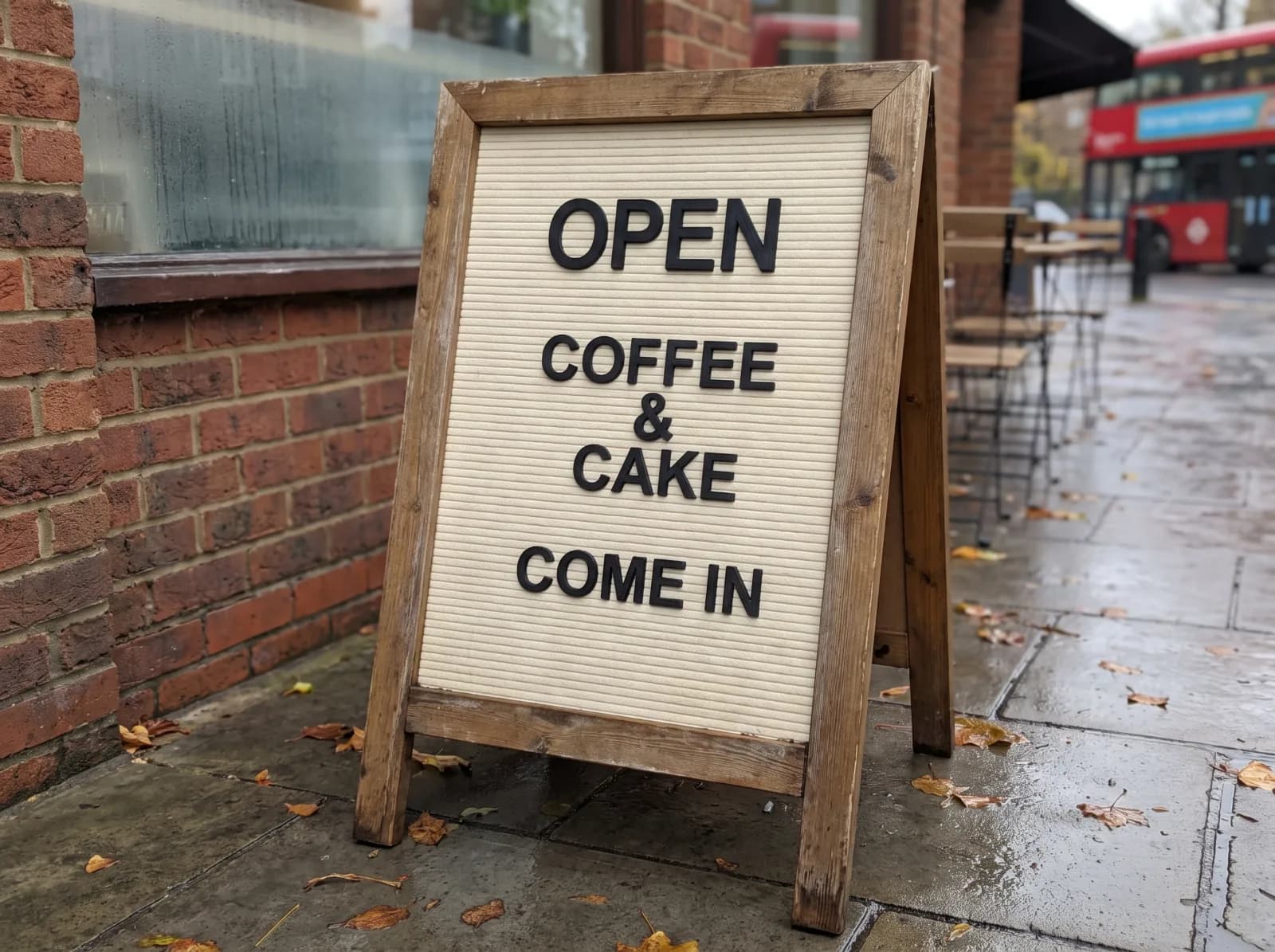 A café A-board on a London pavement reading OPEN, COFFEE & CAKE, COME IN in black 3D-printed letters