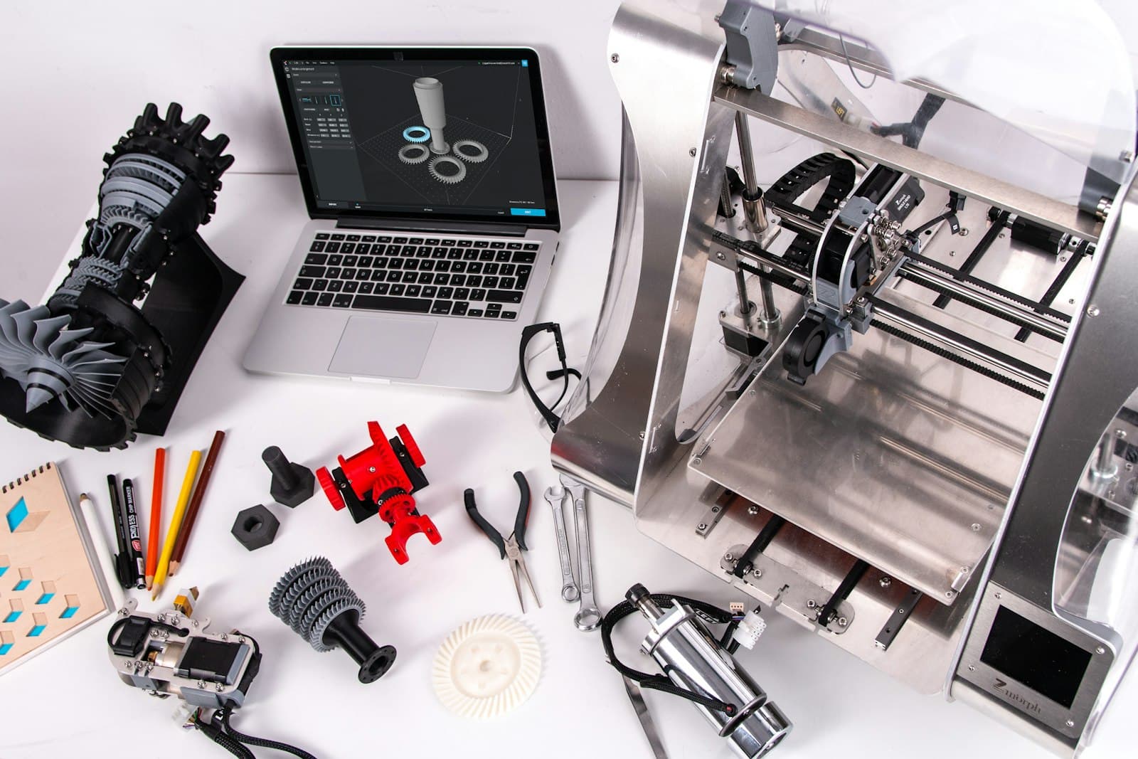 Printed parts, tools and a laptop laid out beside a 3D printer