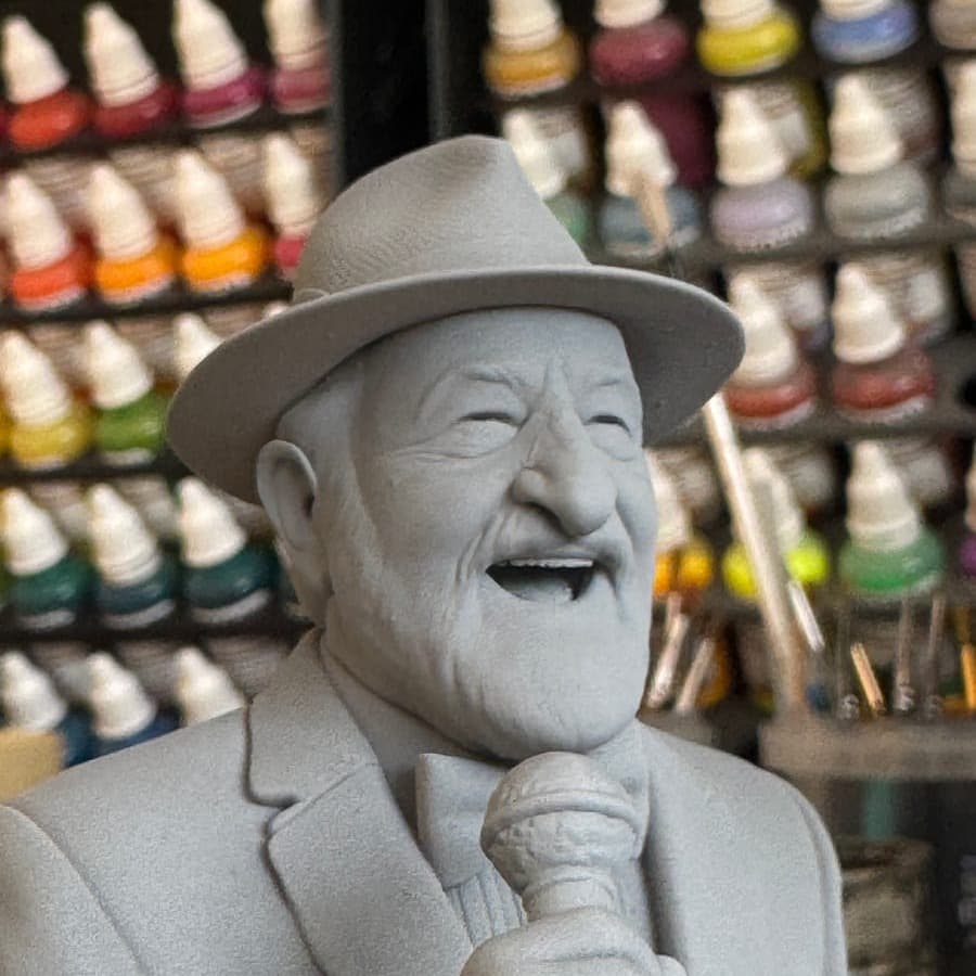 An unpainted resin bust of a laughing man in a hat, singing into a microphone