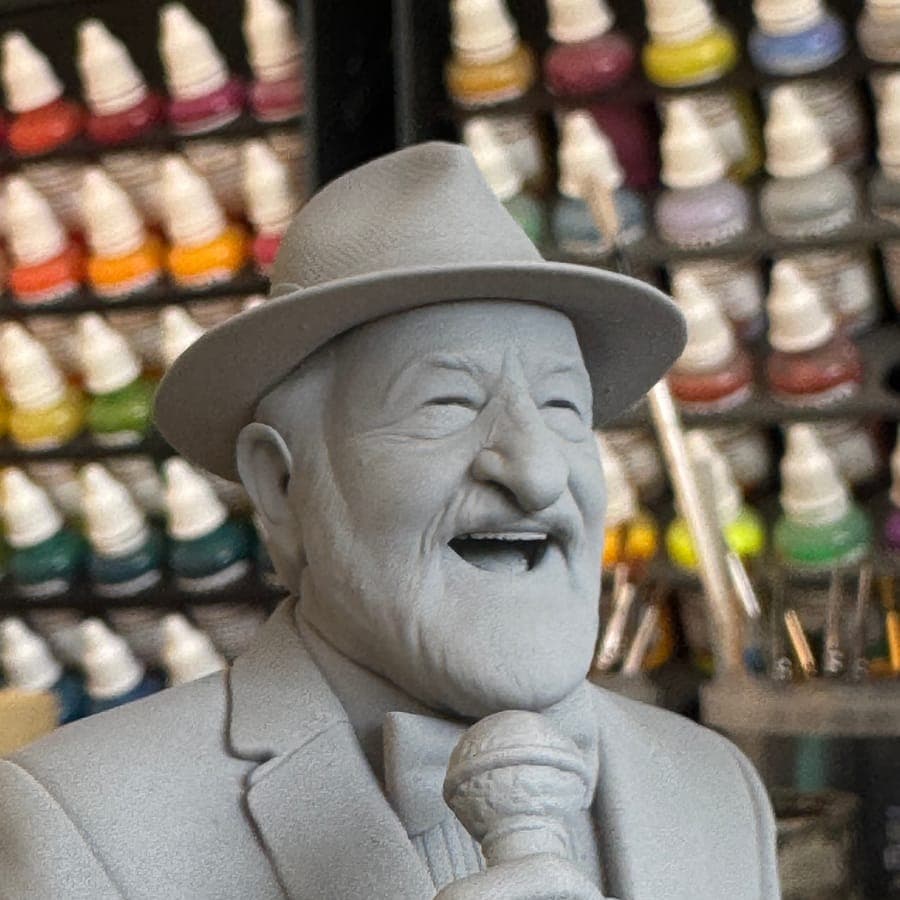 An unpainted resin bust of a laughing man in a hat, singing into a microphone